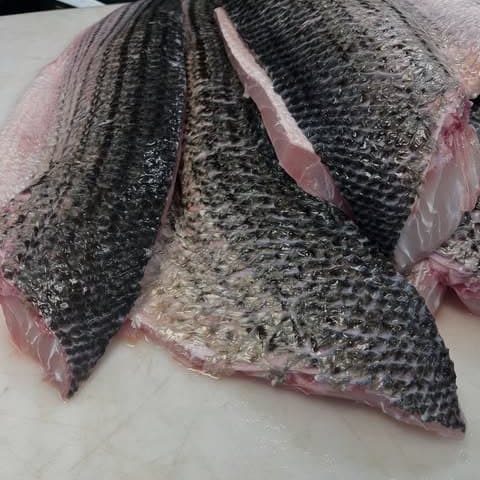 Whole black sea bass, butterflied and laid skin-up on a white cutting board.