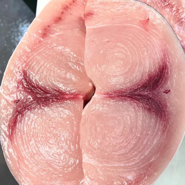 A swordfish steak cut across the loin, the whorled grain and dark bloodline showing.