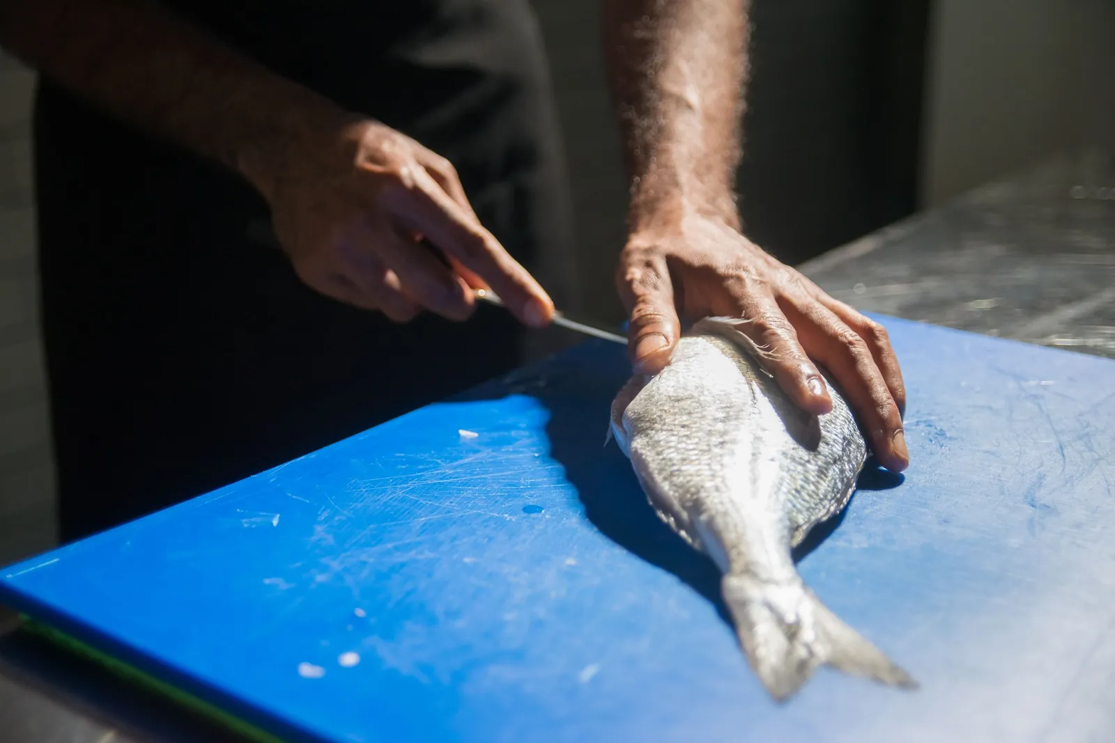 Hands filleting a whole fish on a board at the counter.