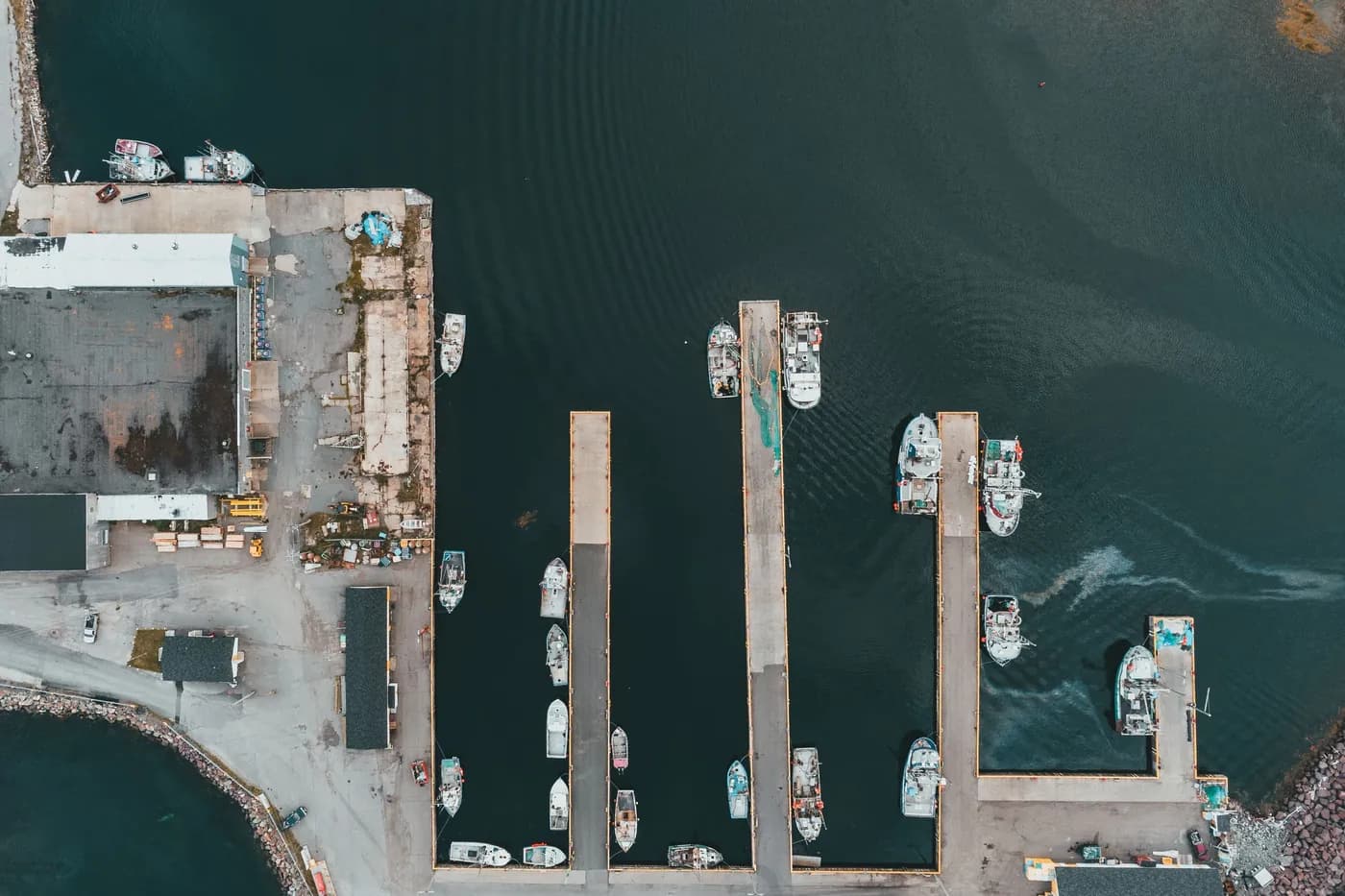A working harbour seen from above, boats tied along the finger docks and a yard behind them.