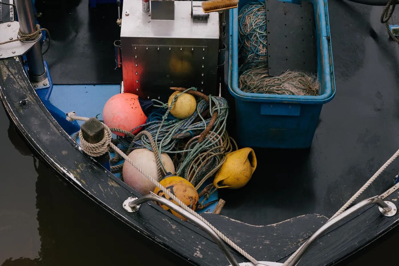 The bow of a small working boat, buoys and coiled rope stowed against a crate of netting.